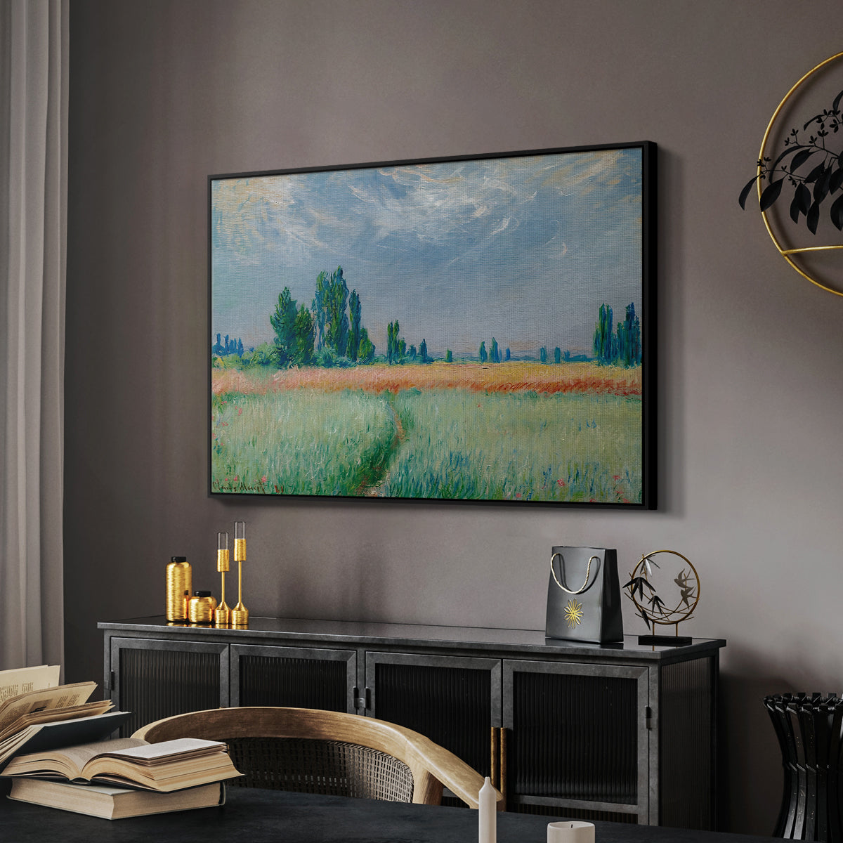The Wheat Field (Champ de Blé), 1881 by Claude Monet in a black floater framed canvas featuring an agricultural landscape with tall wheat and distant horizon, displayed above a desk in a dark home office interior.