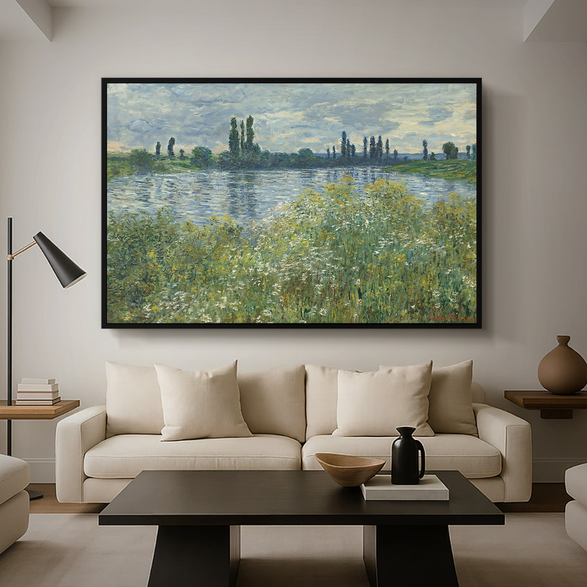 Banks of the Seine, Vétheuil, 1880 by Claude Monet as a black floater framed canvas featuring a riverbank landscape with water, trees, and distant village buildings, displayed above a sofa in a modern living room.