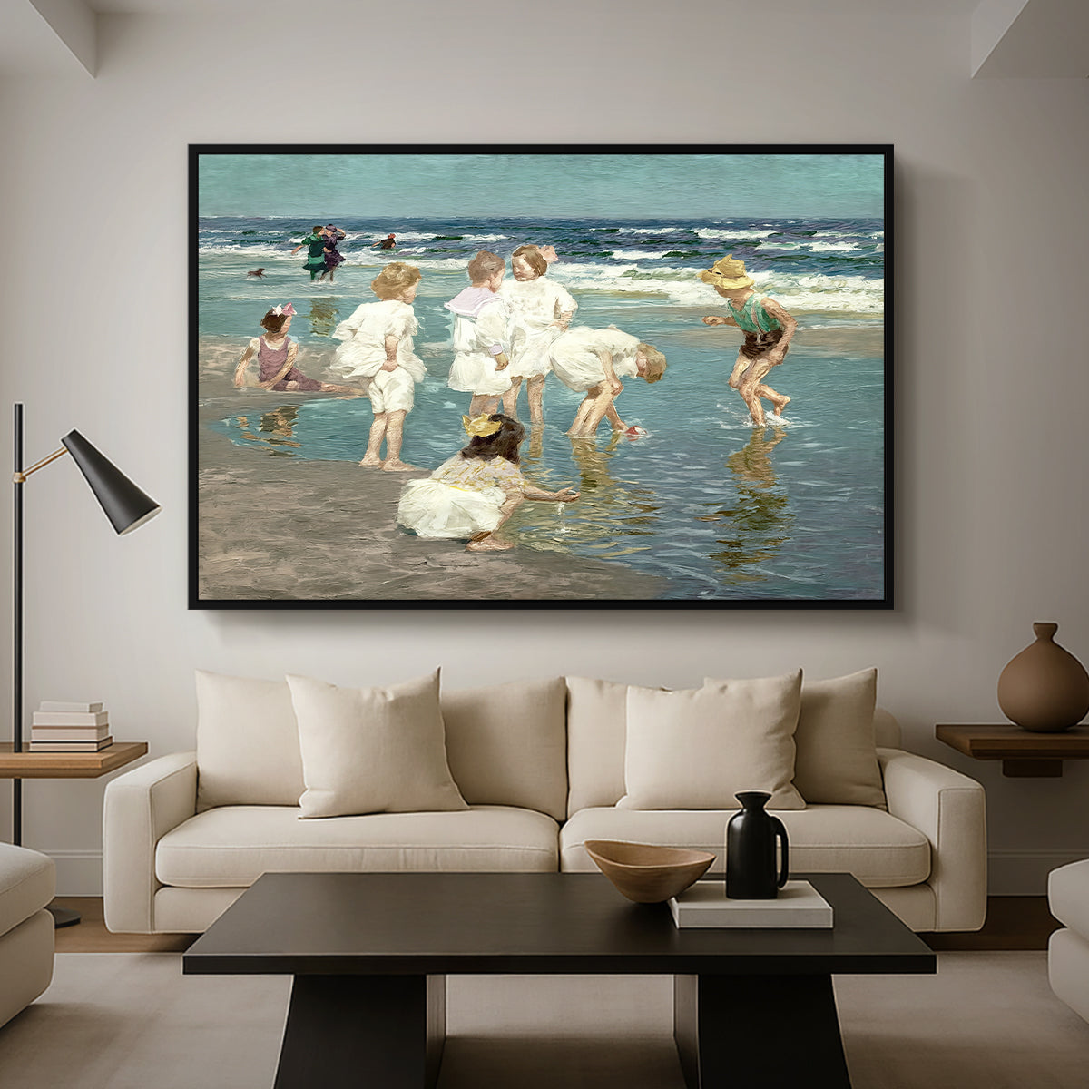 A Holiday, c. 1915 by Edward Henry Potthast as a black floater framed canvas featuring people relaxing and wading in shallow ocean water along a sunny beach, displayed above a sofa in a modern living room.