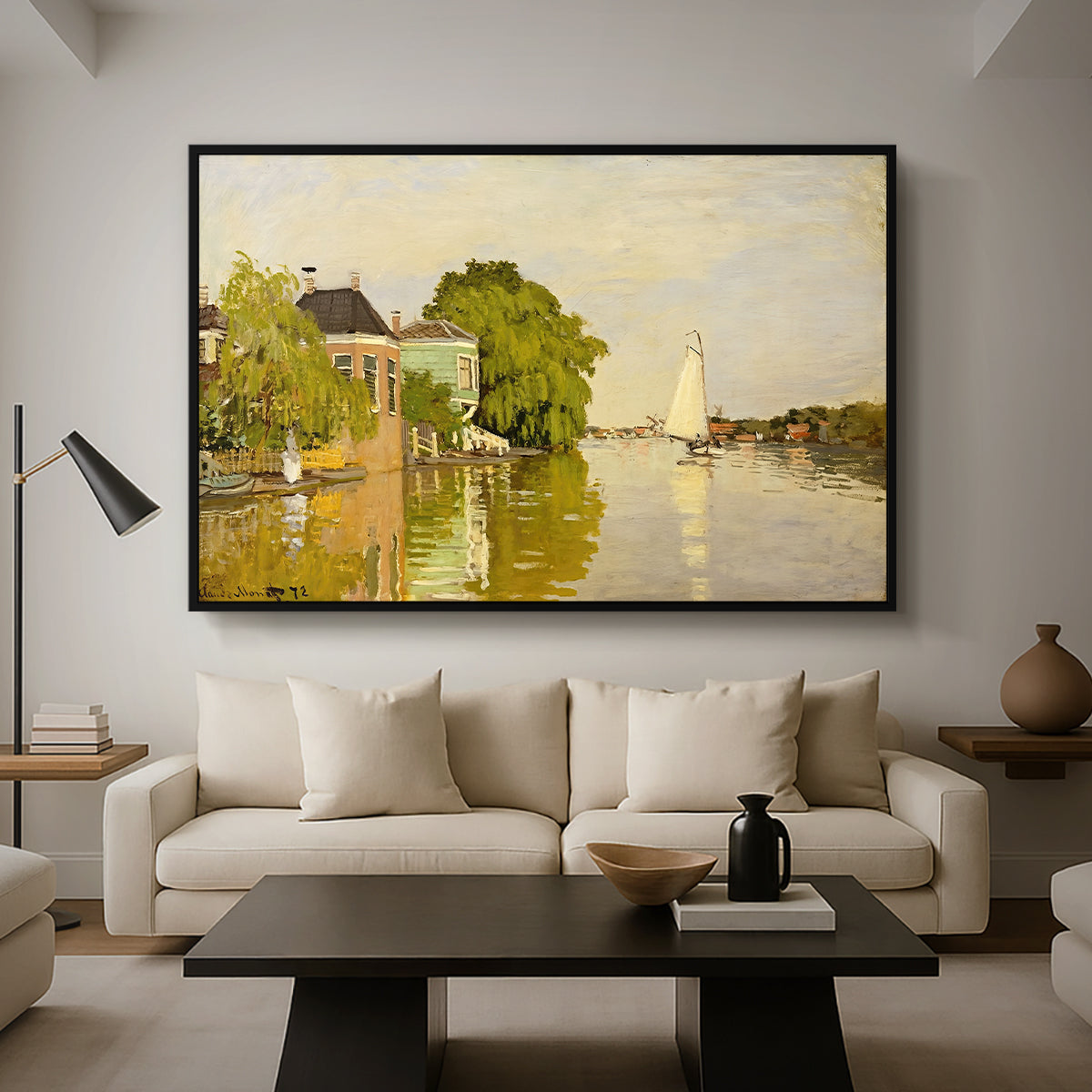 Houses on the Achterzaan, 1871 by Claude Monet as a black floater framed canvas featuring colorful houses reflected in calm river surrounded by greenery, displayed above a sofa in a modern living room.