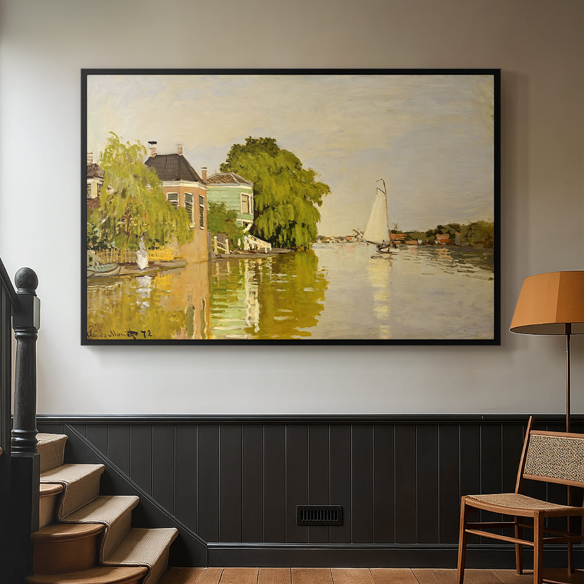 Black floater framed canvas featuring a peaceful village scene with houses bordering water, displayed in a hallway near a staircase.