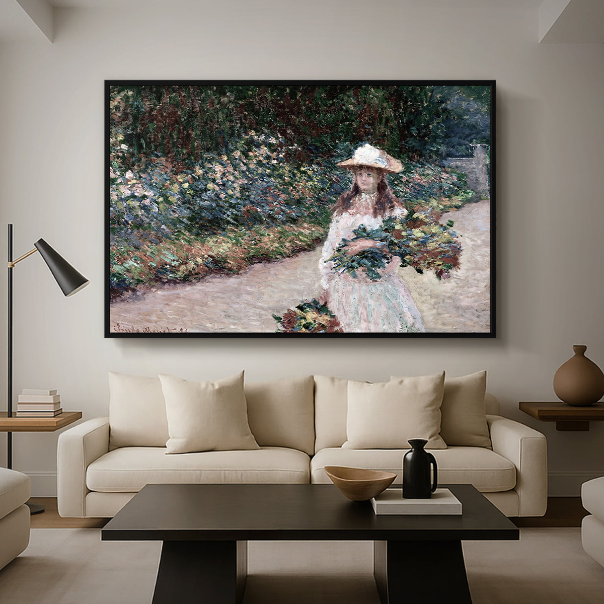 Young Girl in the Garden at Giverny, 1888 by Claude Monet as a black floater framed canvas featuring a young girl seated in lush garden surrounded by blooming flowers, displayed above a sofa in a modern living room.