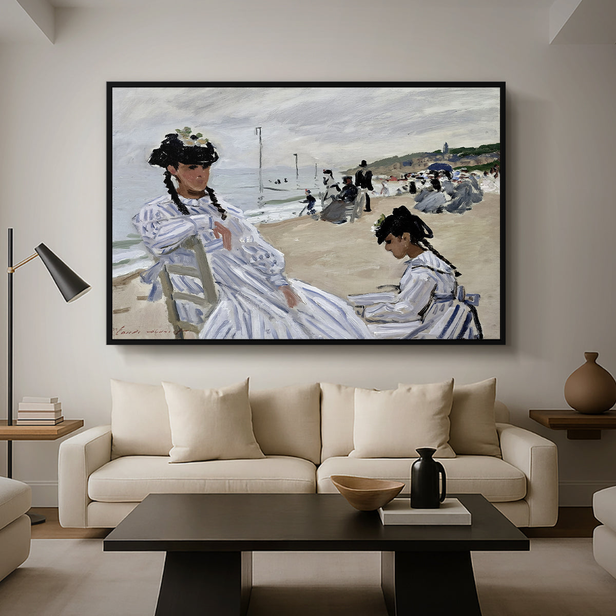 On the Beach at Trouville, 1870 by Claude Monet as a black floater framed canvas featuring figures seated on beach with parasols facing the ocean, displayed above a sofa in a modern living room.