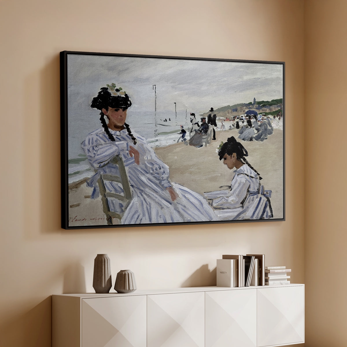 Black floater framed canvas of On the Beach at Trouville, 1870 by Claude Monet, featuring an impressionist seaside scene with women in dresses and hats above a console cabinet in a minimalist entryway.
