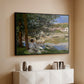 Black floater framed canvas of On the Bank of the Seine, Bennecourt, 1868 by Claude Monet, featuring a peaceful riverside scene with figures resting in grassy area by water above a console cabinet in a minimalist entryway.