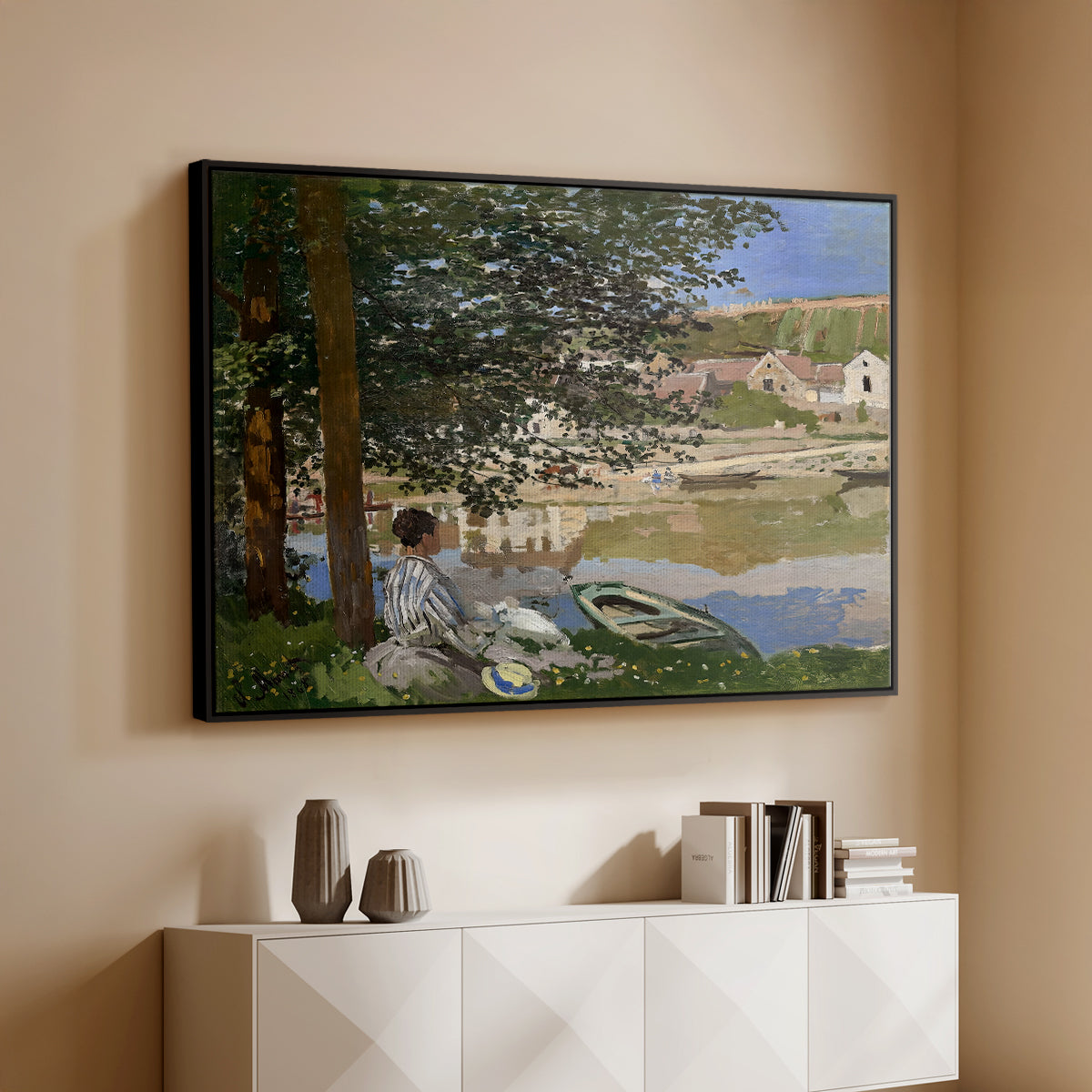 Black floater framed canvas of On the Bank of the Seine, Bennecourt, 1868 by Claude Monet, featuring a peaceful riverside scene with figures resting in grassy area by water above a console cabinet in a minimalist entryway.