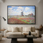 Tulip Fields with the Rijnsburg Windmill, 1886 by Claude Monet as a black floater framed canvas featuring colorful rows of tulip fields leading toward distant windmill, displayed above a sofa in a modern living room.