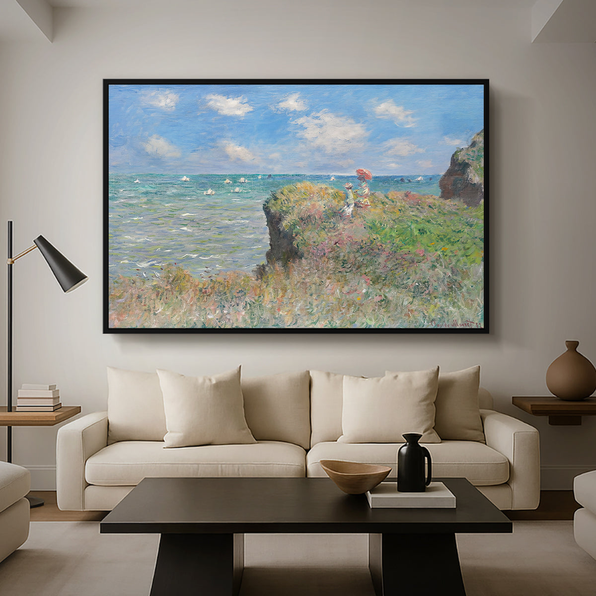 The Cliff Walk at Pourville, 1882 by Claude Monet as a black floater framed canvas featuring figures walking along coastal cliff path overlooking ocean and sky, displayed above a sofa in a modern living room.