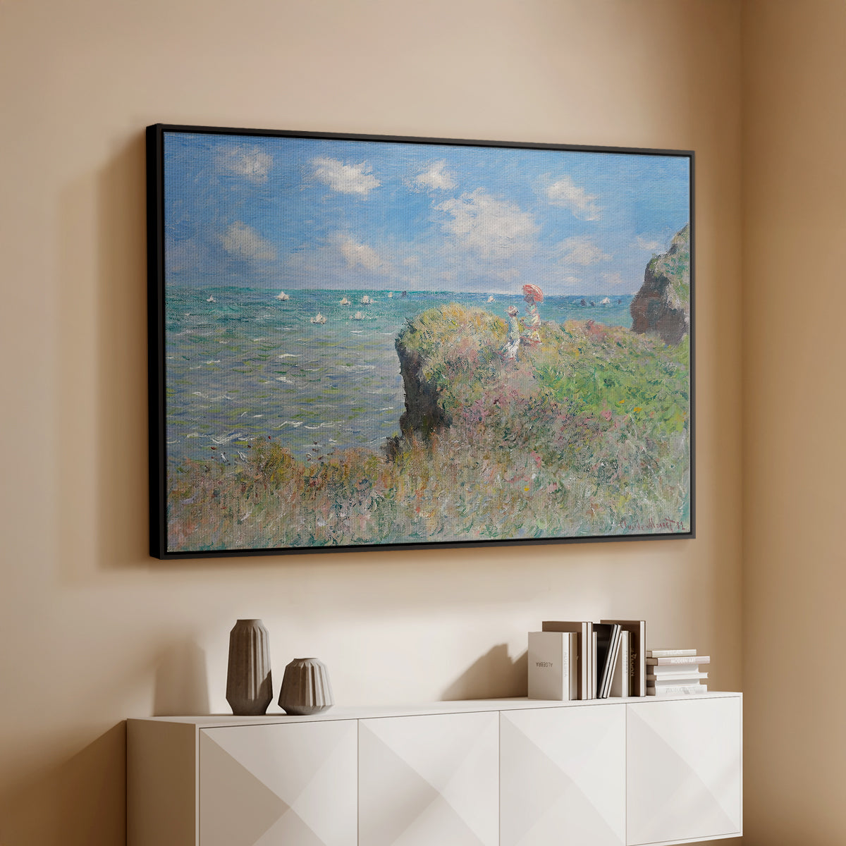 Black floater framed canvas of The Cliff Walk at Pourville, 1882 by Claude Monet, featuring an impressionist seaside landscape with people strolling above water above a console cabinet in a minimalist entryway.