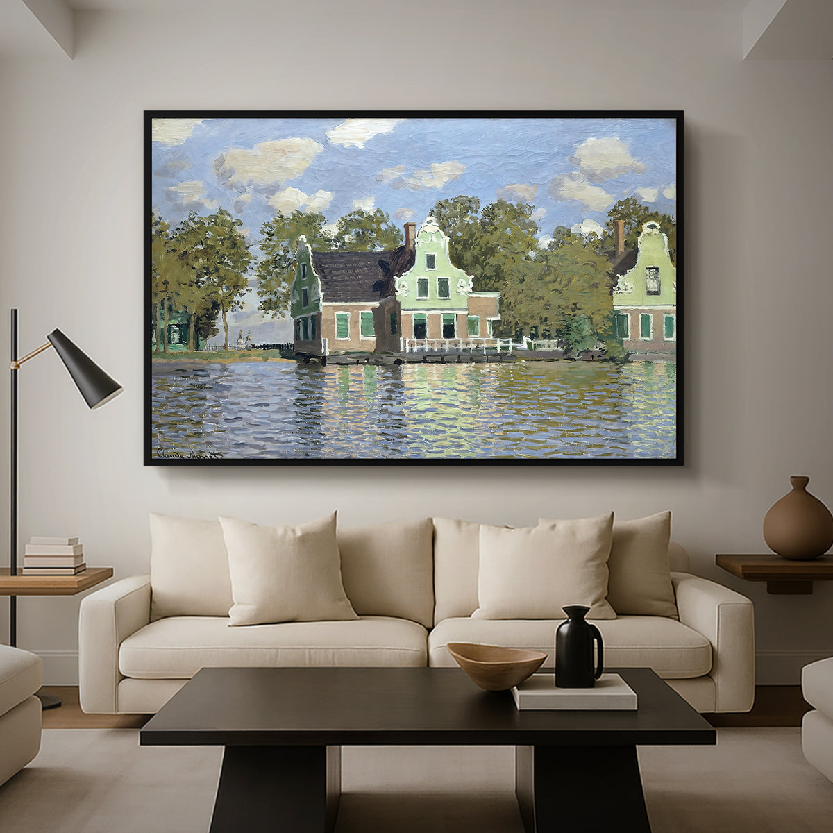 Houses on the Zaan River at Zaandam, 1871 by Claude Monet as a black floater framed canvas featuring a row of houses along river with reflections in calm water, displayed above a sofa in a modern living room.