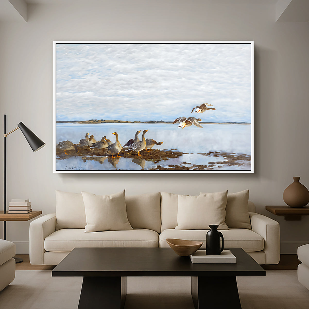 Greylag Geese (Grågäss), 1922 by Bruno Liljefors as a white floater framed canvas featuring a group of geese gathered near water in a natural wetland landscape, displayed above a sofa in a modern living room.