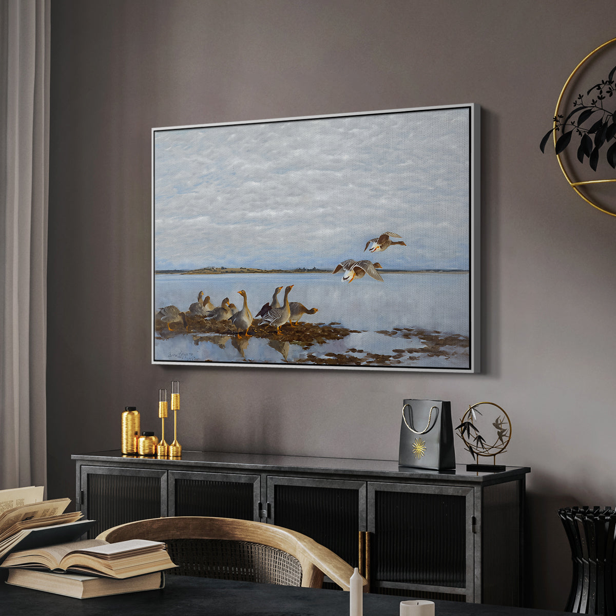 Greylag Geese (Grågäss), 1922 by Bruno Liljefors in a white floater framed canvas featuring a realistic wildlife scene of geese in calm outdoor environment, displayed above a desk in a dark home office interior.