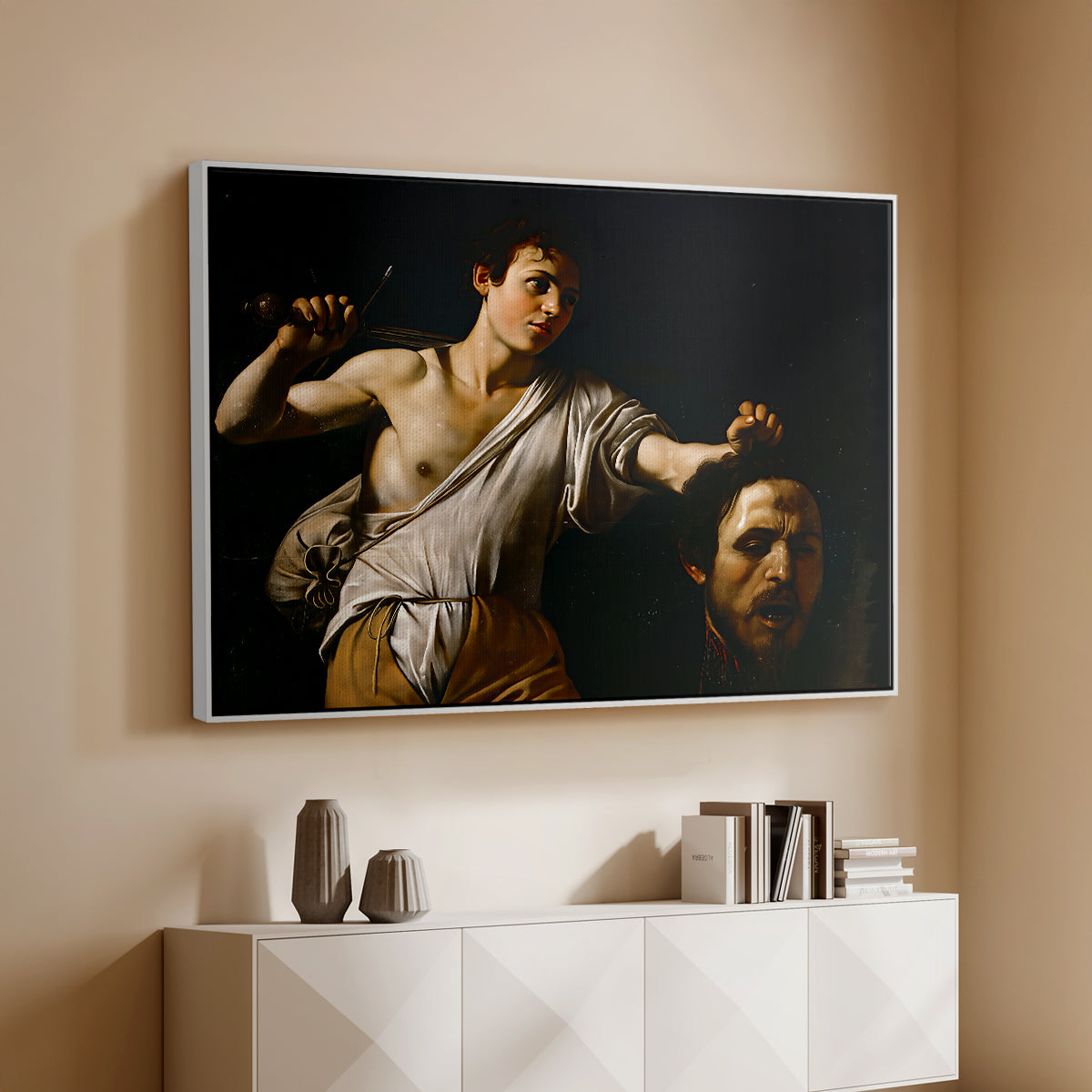White floater framed canvas of David with the Head of Goliath (Vienna Version), c. 1607 by Caravaggio, featuring a biblical scene of David gripping Goliath's head with dramatic lighting above a console cabinet in a minimalist entryway.