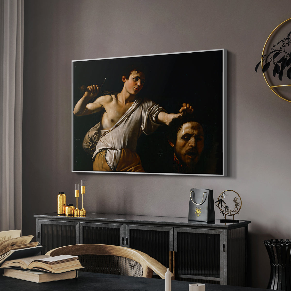 David with the Head of Goliath (Vienna Version), c. 1607 by Caravaggio in a white floater framed canvas featuring a Baroque depiction of youth holding severed head in shadowy setting, displayed above a desk in a dark home office interior.