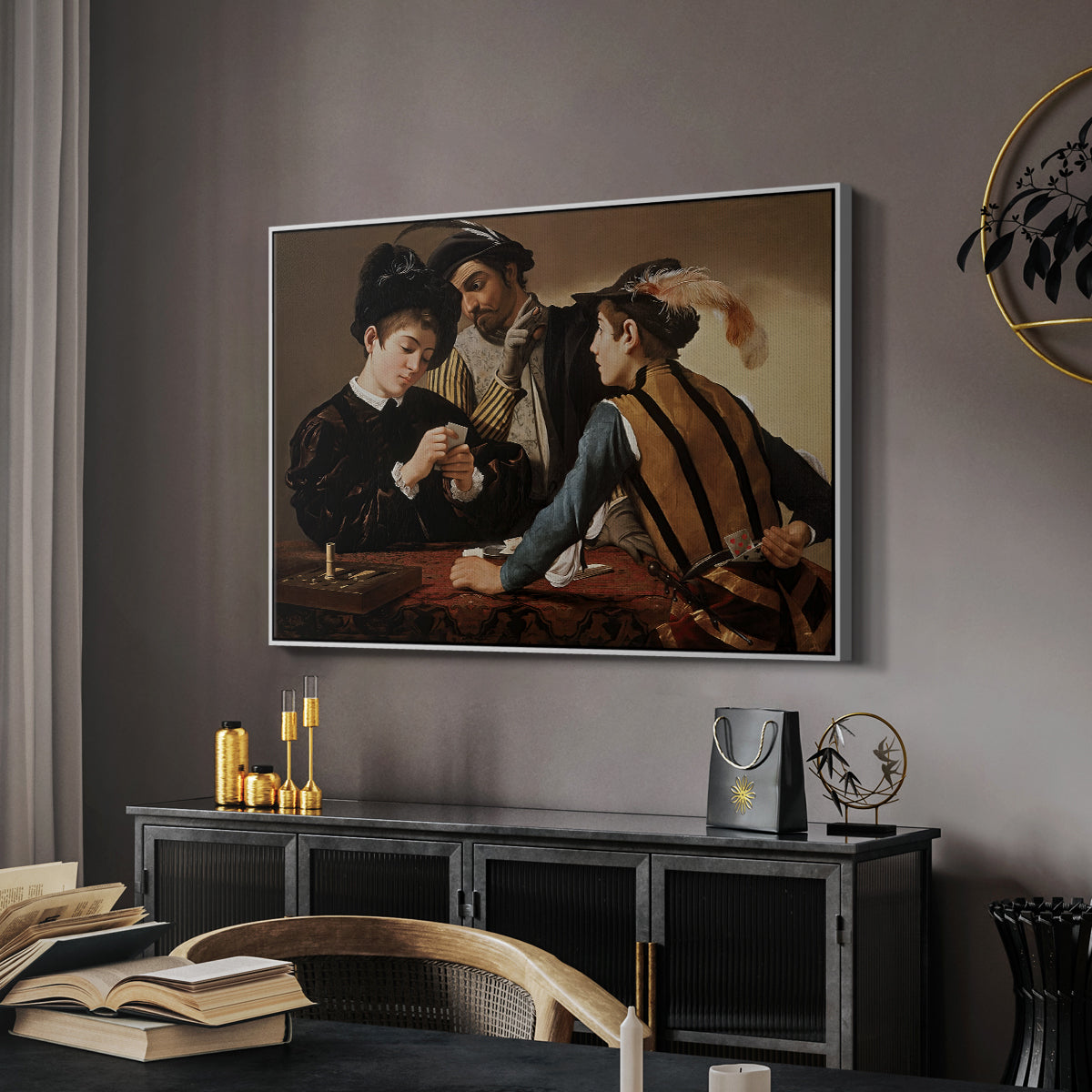 The Cardsharps, c. 1594 by Caravaggio in a white floater framed canvas featuring a young men playing cards with one cheating and another watching closely, displayed above a desk in a dark home office interior.