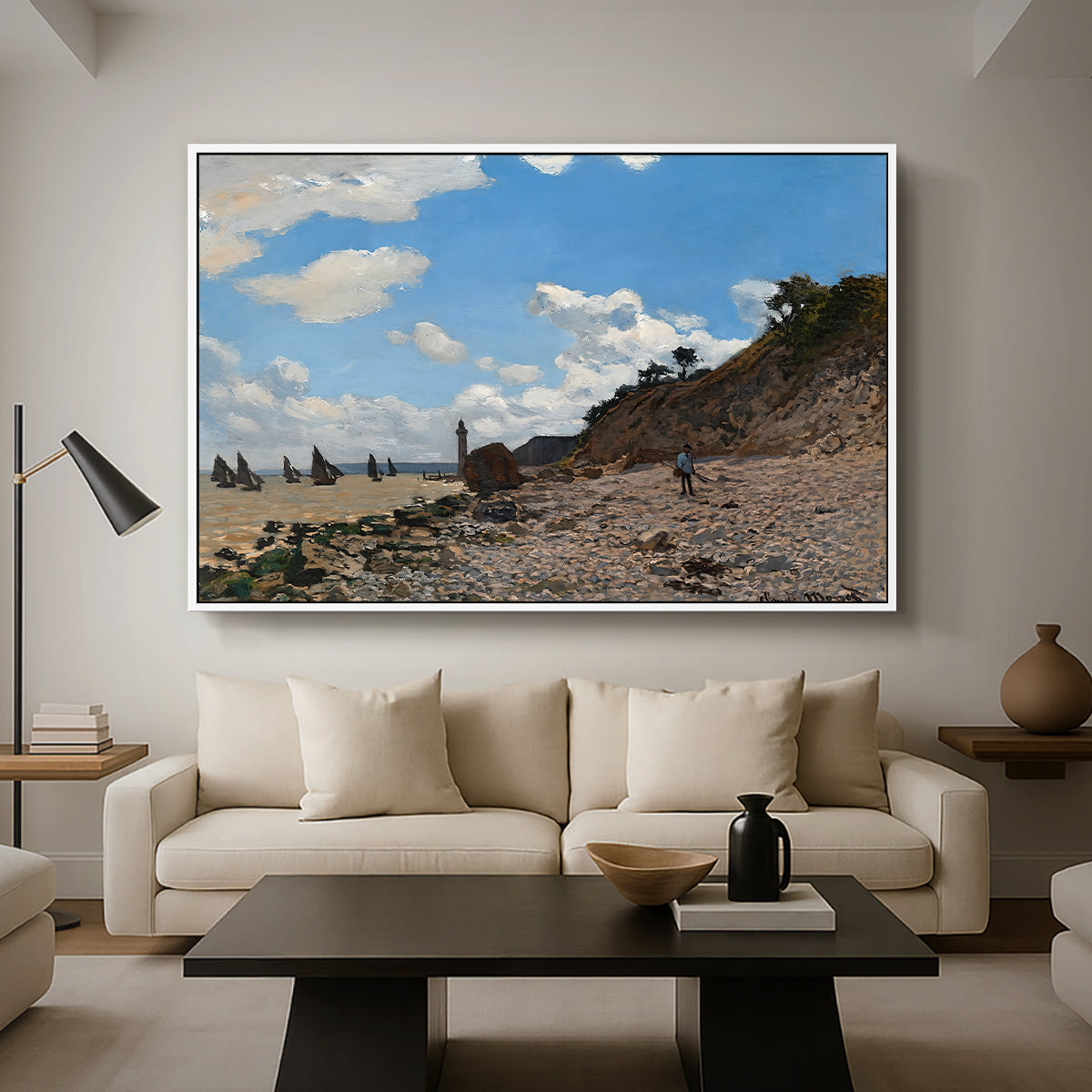 The Beach at Honfleur, 1864 by Claude Monet as a white floater framed canvas featuring a coastal beach scene with figures gathered along shoreline and boats nearby, displayed above a sofa in a modern living room.