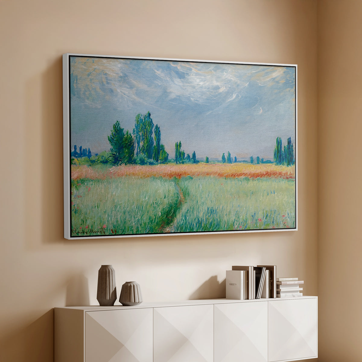 White floater framed canvas of The Wheat Field (Champ de Blé), 1881 by Claude Monet, featuring an impressionist depiction of ripened grain field in countryside above a console cabinet in a minimalist entryway.
