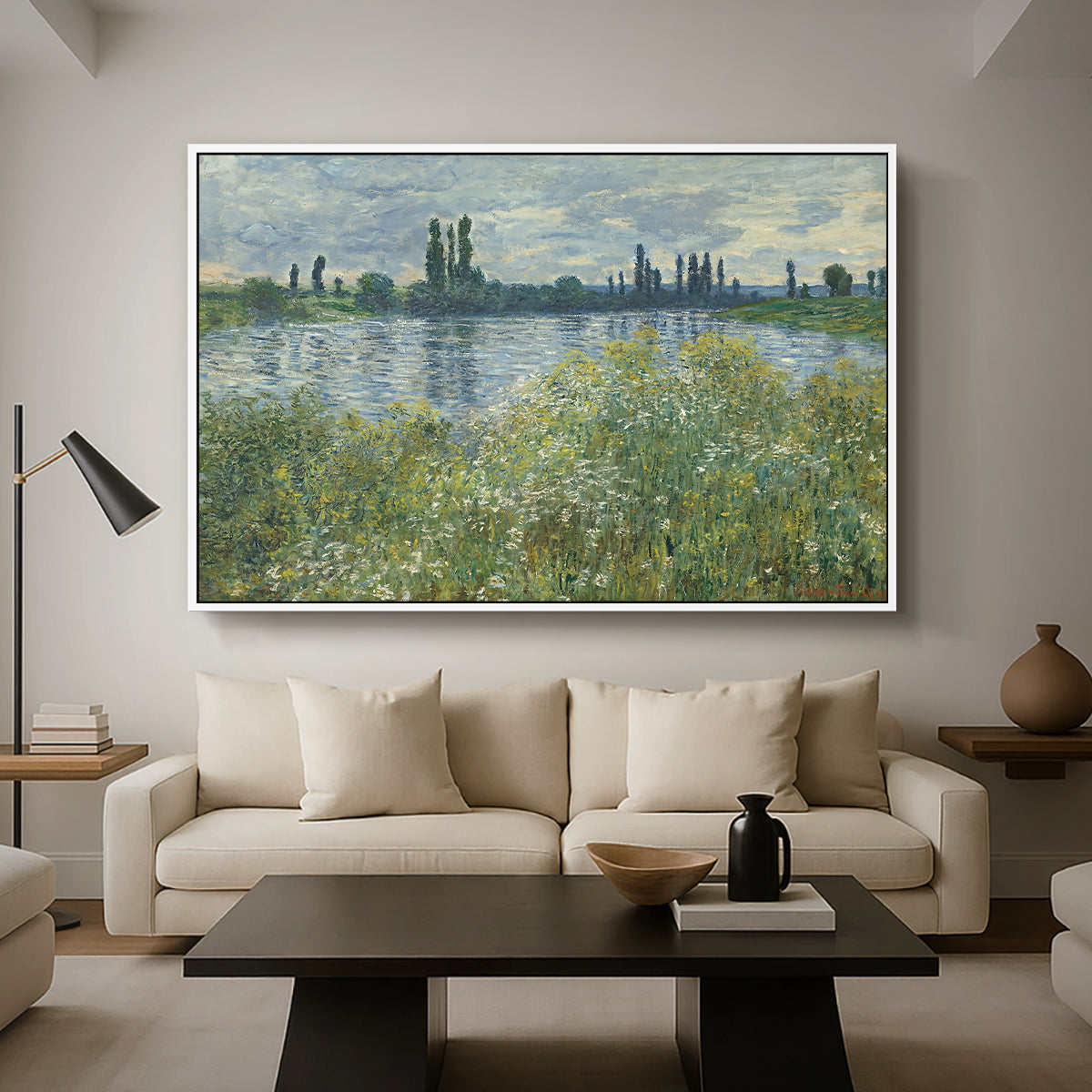 Banks of the Seine, Vétheuil, 1880 by Claude Monet as a white floater framed canvas featuring a riverbank landscape with water, trees, and distant village buildings, displayed above a sofa in a modern living room.
