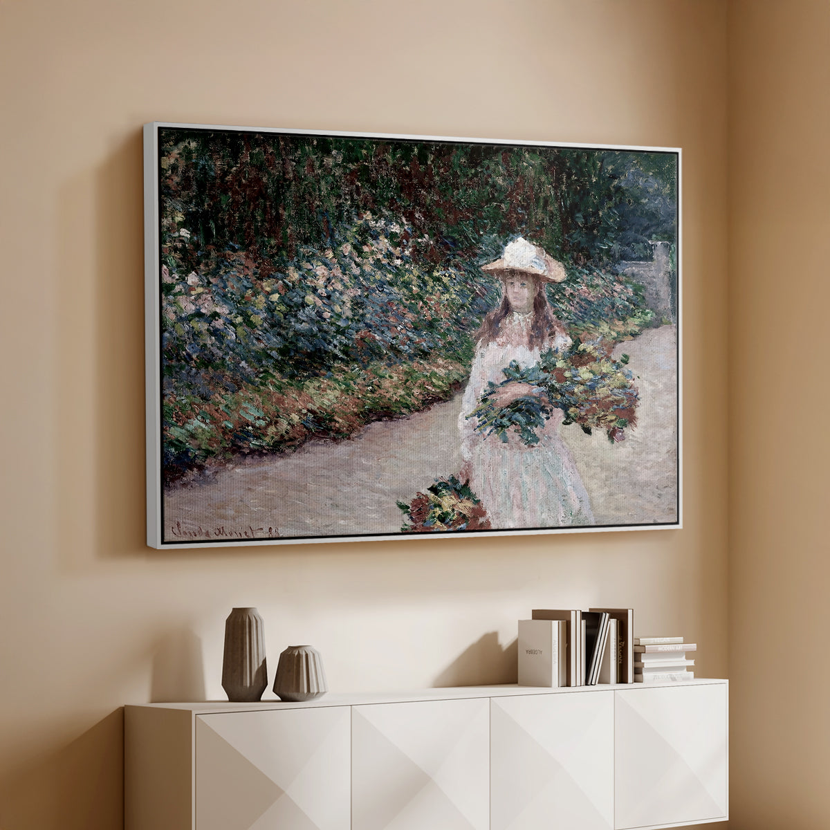 White floater framed canvas of Young Girl in the Garden at Giverny, 1888 by Claude Monet, featuring an impressionist garden scene with child among greenery and blossoms above a console cabinet in a minimalist entryway.