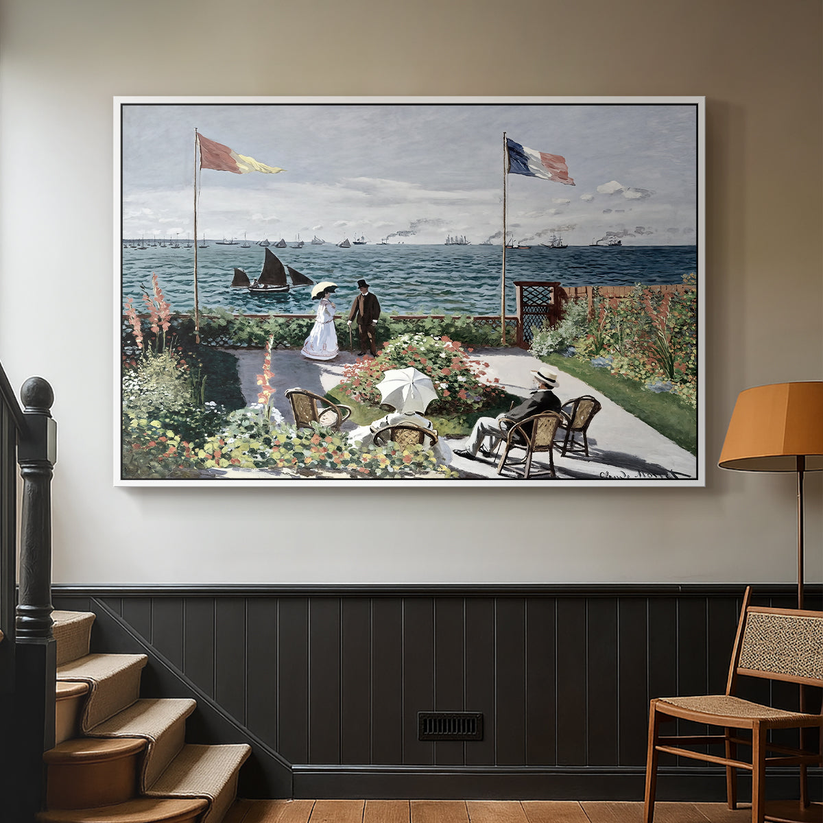 White floater framed canvas featuring a landscaped terrace with figures and flags near shoreline, displayed in a hallway near a staircase.