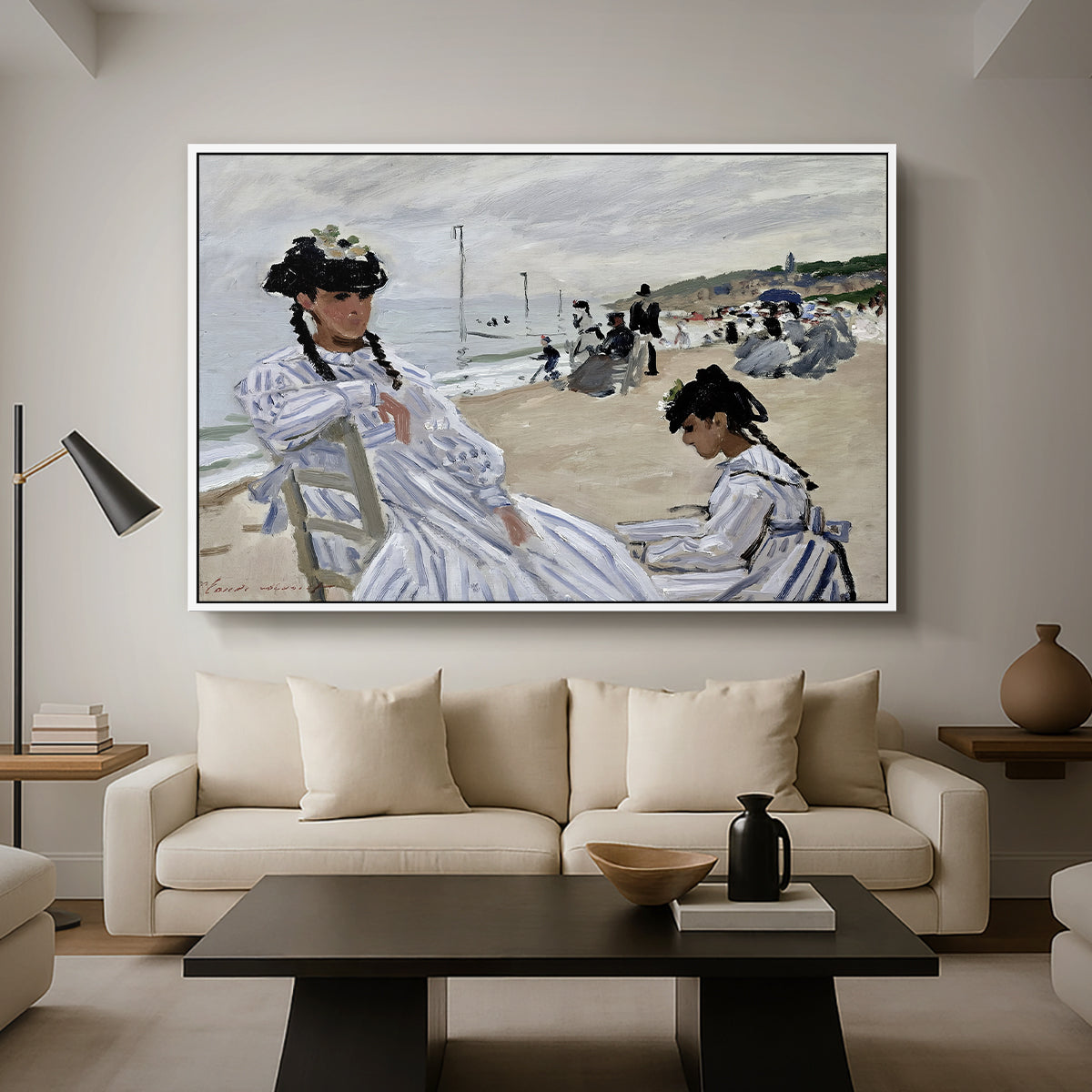 On the Beach at Trouville, 1870 by Claude Monet as a white floater framed canvas featuring figures seated on beach with parasols facing the ocean, displayed above a sofa in a modern living room.