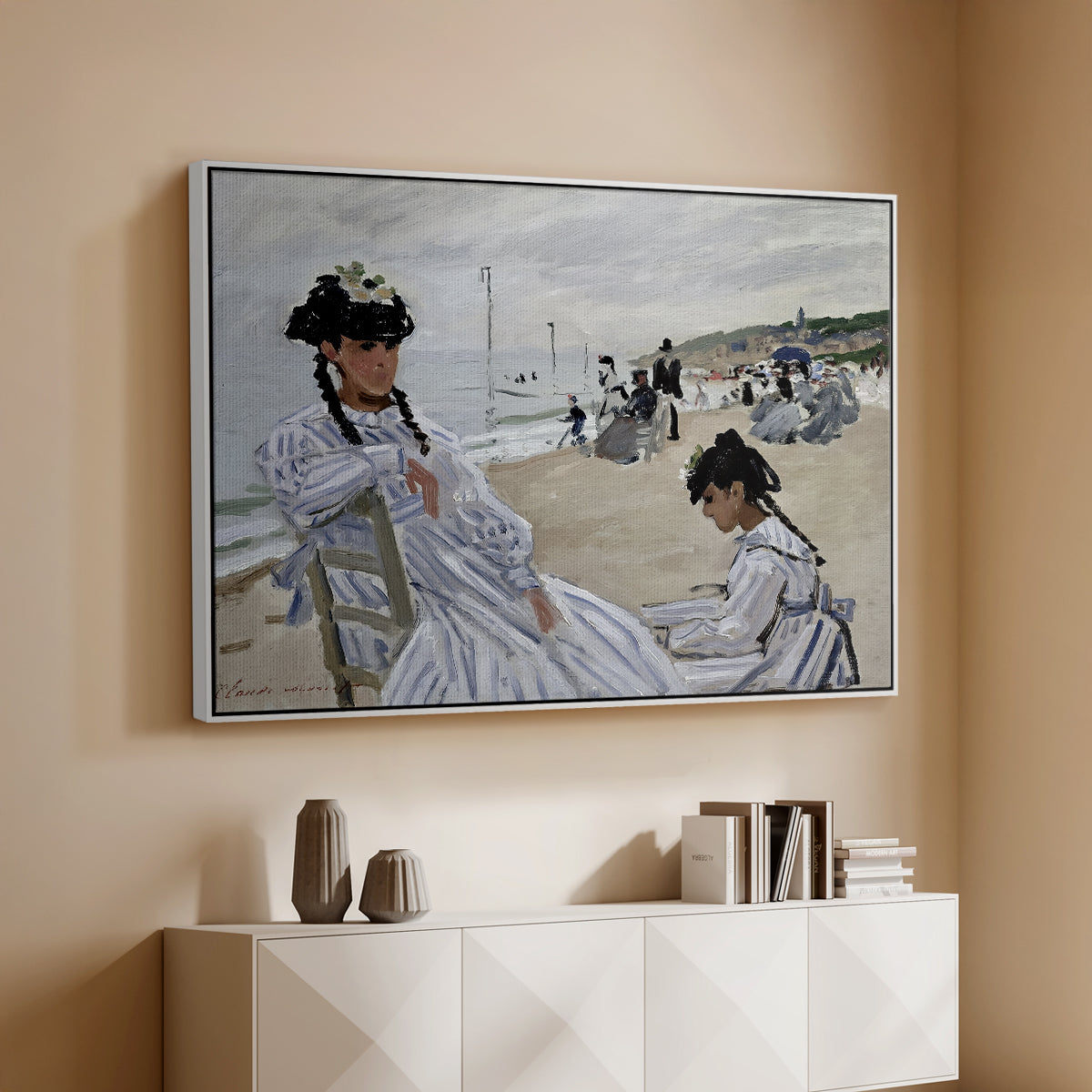 White floater framed canvas of On the Beach at Trouville, 1870 by Claude Monet, featuring an impressionist seaside scene with women in dresses and hats above a console cabinet in a minimalist entryway.
