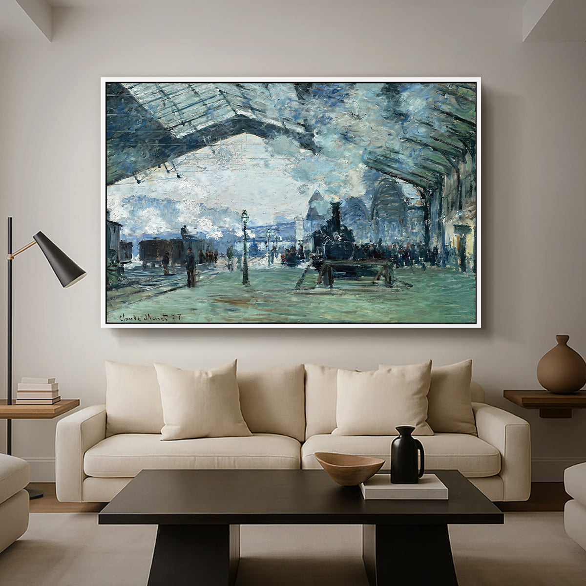 The Saint-Lazare Station, 1877 by Claude Monet as a white floater framed canvas featuring trains arriving under large arched station roof with billowing steam, displayed above a sofa in a modern living room.