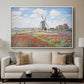 Tulip Fields with the Rijnsburg Windmill, 1886 by Claude Monet displayed in a white floater framed canvas above a sofa in a clean living room.