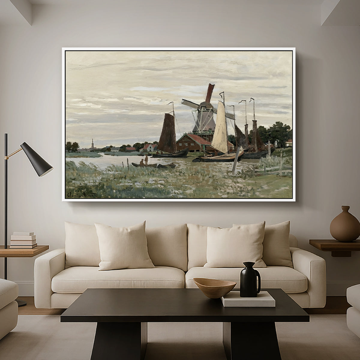 Windmill at Zaandam, 1871 by Claude Monet as a white floater framed canvas featuring a single windmill beside water with surrounding buildings and sky, displayed above a sofa in a modern living room.