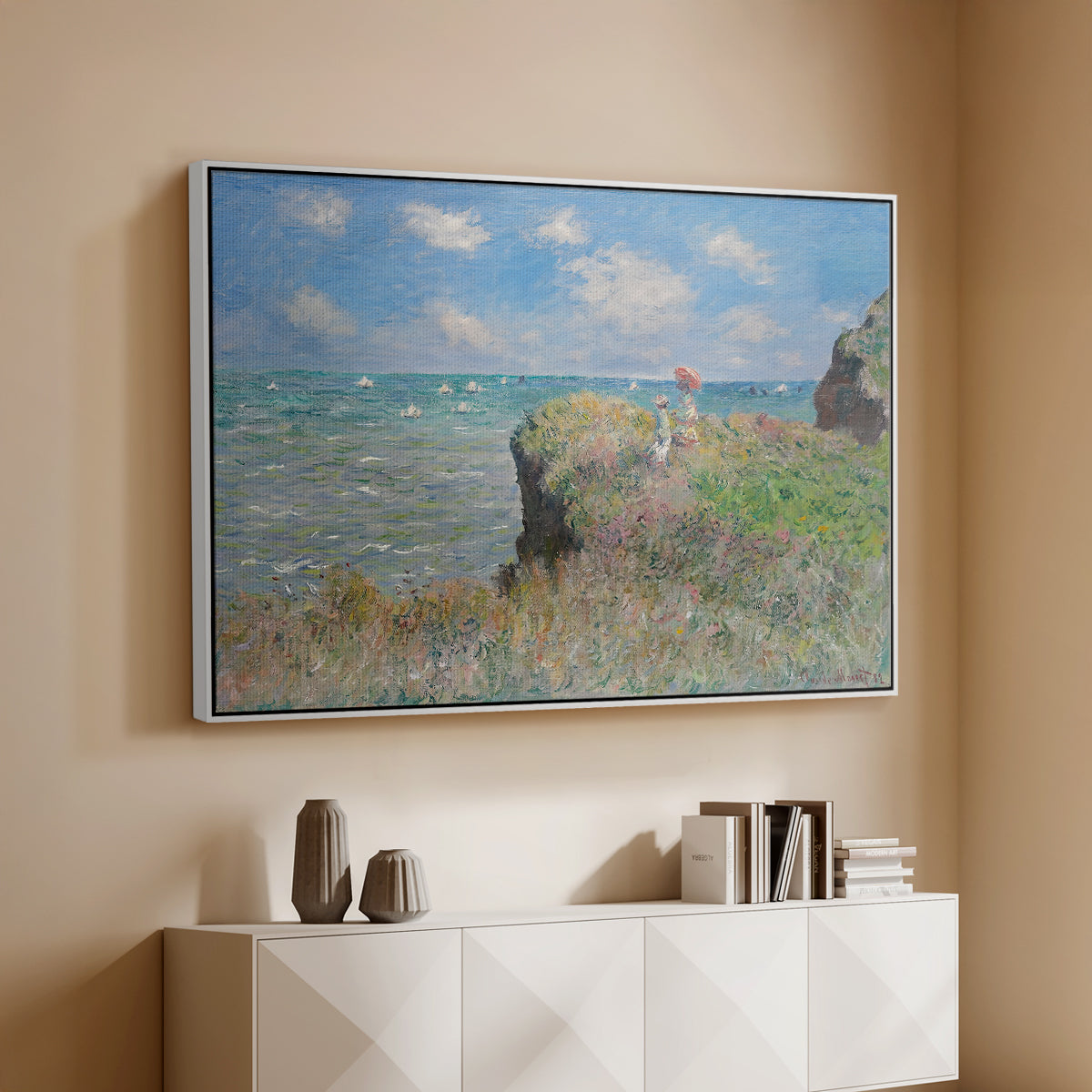 White floater framed canvas of The Cliff Walk at Pourville, 1882 by Claude Monet, featuring an impressionist seaside landscape with people strolling above water above a console cabinet in a minimalist entryway.