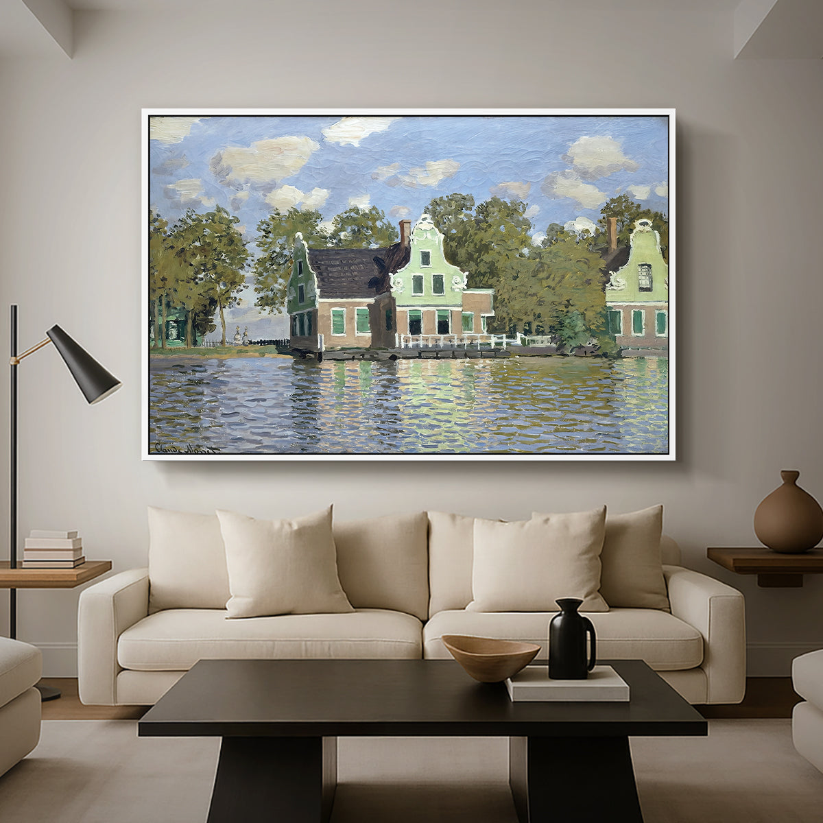 Houses on the Zaan River at Zaandam, 1871 by Claude Monet as a white floater framed canvas featuring a row of houses along river with reflections in calm water, displayed above a sofa in a modern living room.