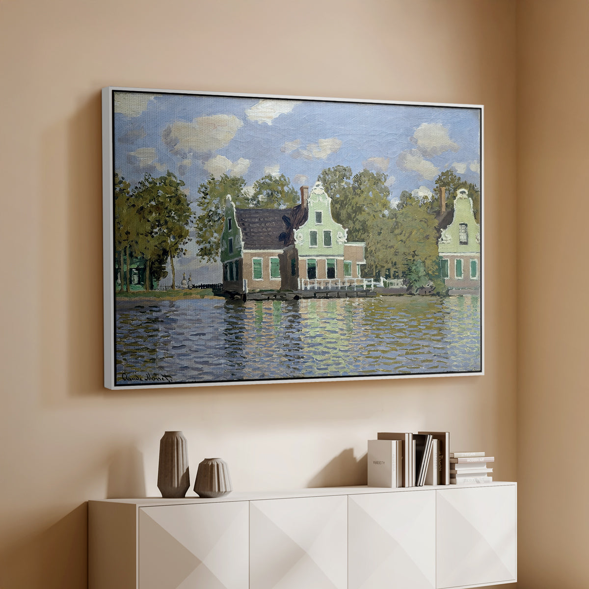 White floater framed canvas of Houses on the Zaan River at Zaandam, 1871 by Claude Monet, featuring an impressionist riverside village with colorful buildings above a console cabinet in a minimalist entryway.
