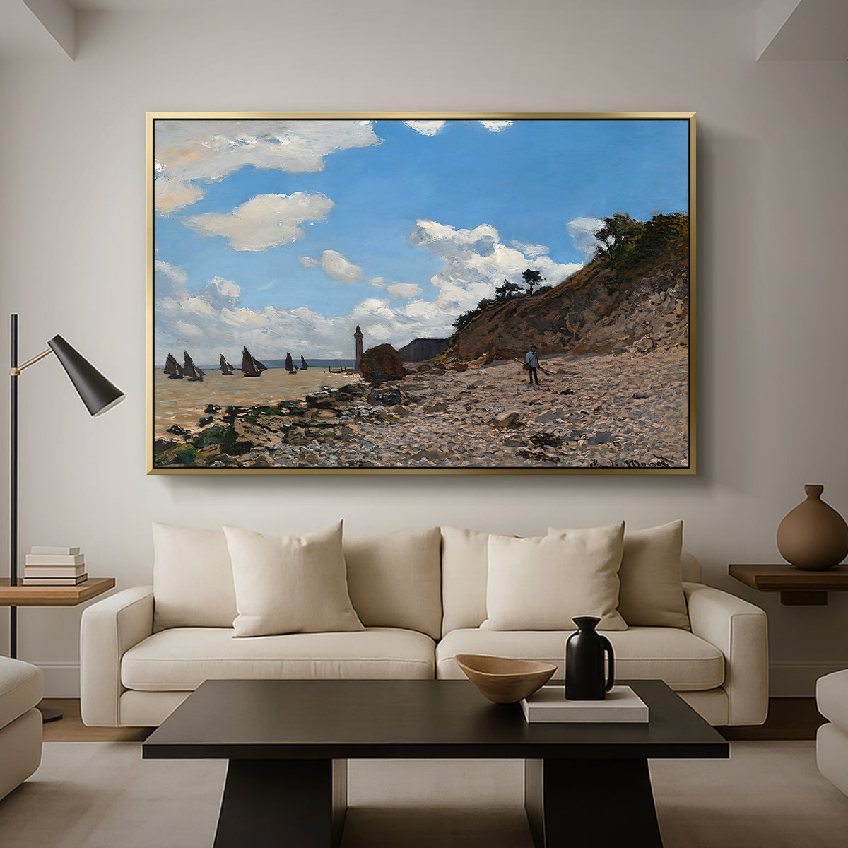 The Beach at Honfleur, 1864 by Claude Monet as a gold floater framed canvas featuring a coastal beach scene with figures gathered along shoreline and boats nearby, displayed above a sofa in a modern living room.