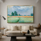 The Wheat Field (Champ de Blé), 1881 by Claude Monet as a gold floater framed canvas featuring a golden wheat field stretching across landscape under soft sky, displayed above a sofa in a modern living room.