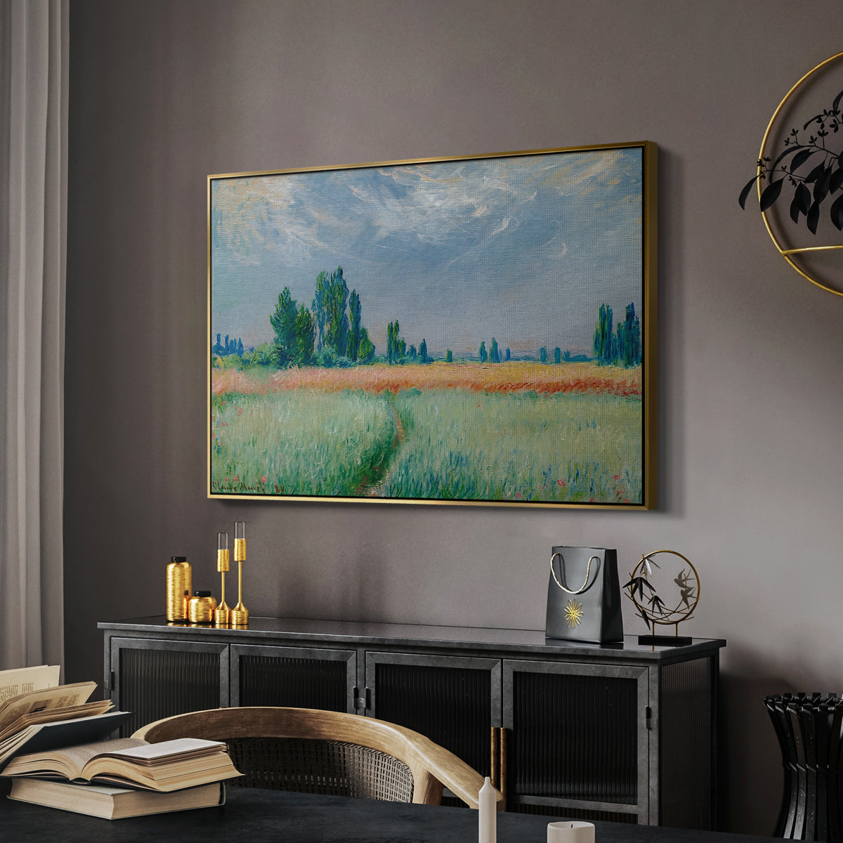 The Wheat Field (Champ de Blé), 1881 by Claude Monet in a gold floater framed canvas featuring an agricultural landscape with tall wheat and distant horizon, displayed above a desk in a dark home office interior.
