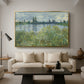 Banks of the Seine, Vétheuil, 1880 by Claude Monet as a gold floater framed canvas featuring a riverbank landscape with water, trees, and distant village buildings, displayed above a sofa in a modern living room.