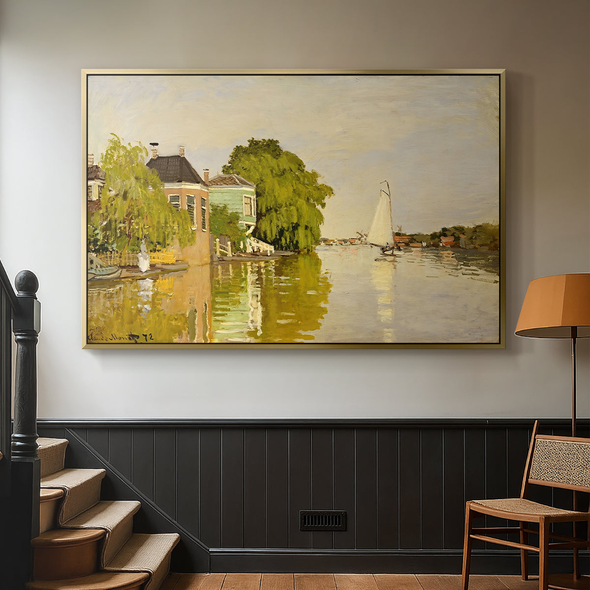 Gold floater framed canvas featuring a peaceful village scene with houses bordering water, displayed in a hallway near a staircase.
