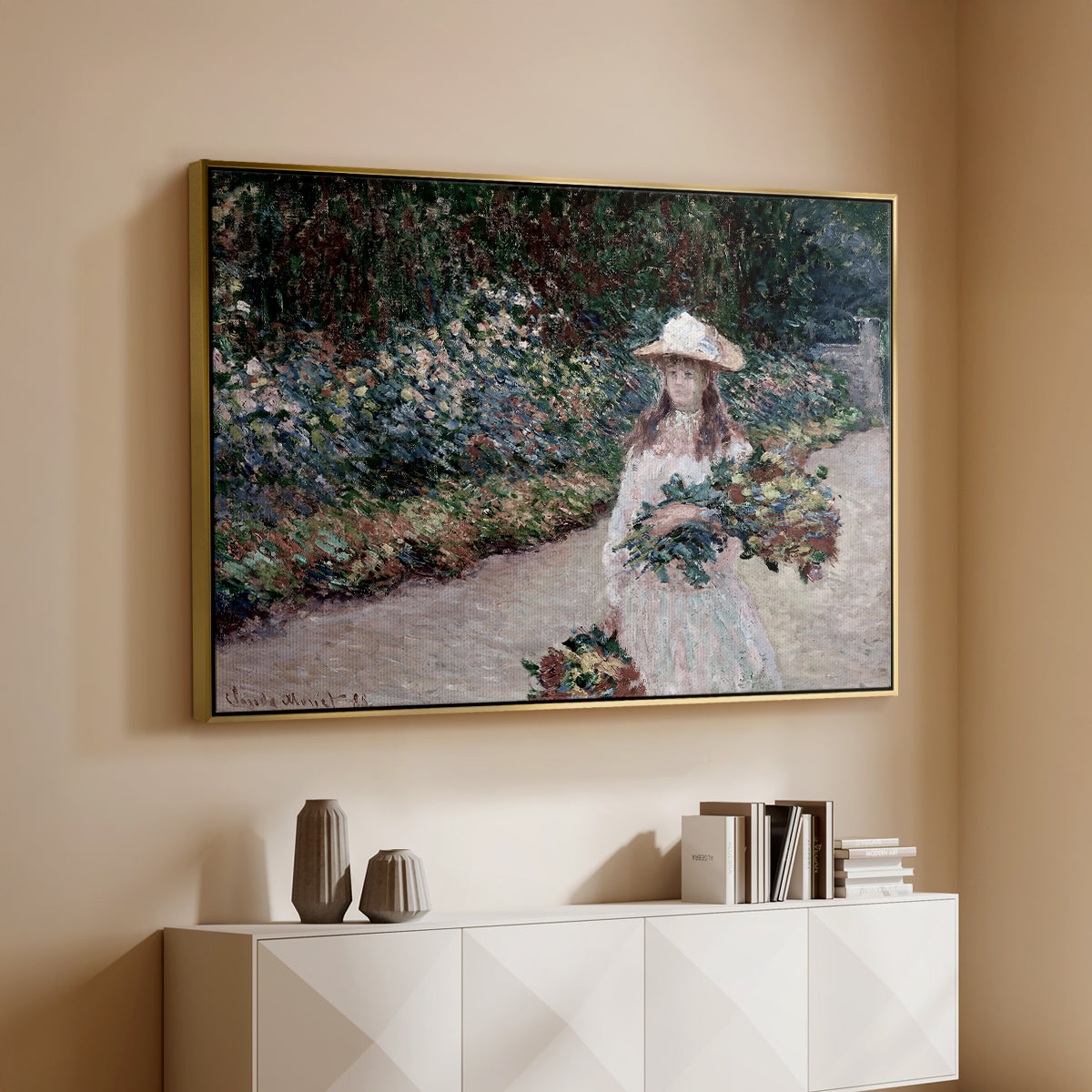 Gold floater framed canvas of Young Girl in the Garden at Giverny, 1888 by Claude Monet, featuring an impressionist garden scene with child among greenery and blossoms above a console cabinet in a minimalist entryway.