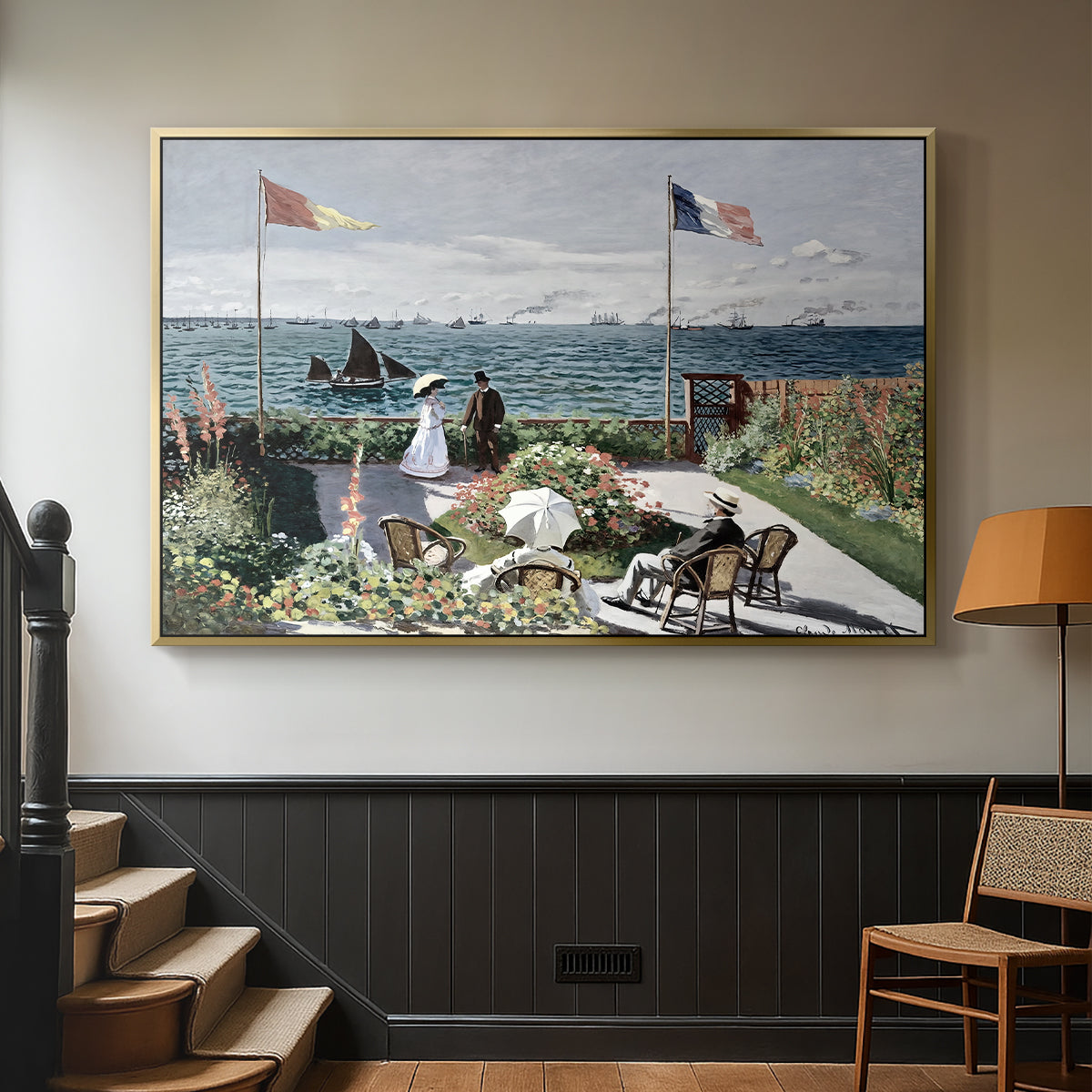 Gold floater framed canvas featuring a landscaped terrace with figures and flags near shoreline, displayed in a hallway near a staircase.