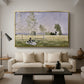 Summer (L'ete), 1874 by Claude Monet as a gold floater framed canvas featuring a woman seated in grassy field beneath tree in bright summer landscape, displayed above a sofa in a modern living room.