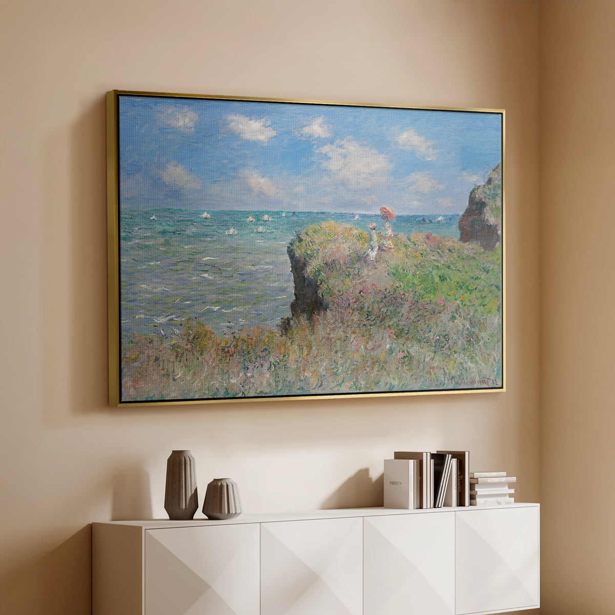 Gold floater framed canvas of The Cliff Walk at Pourville, 1882 by Claude Monet, featuring an impressionist seaside landscape with people strolling above water above a console cabinet in a minimalist entryway.
