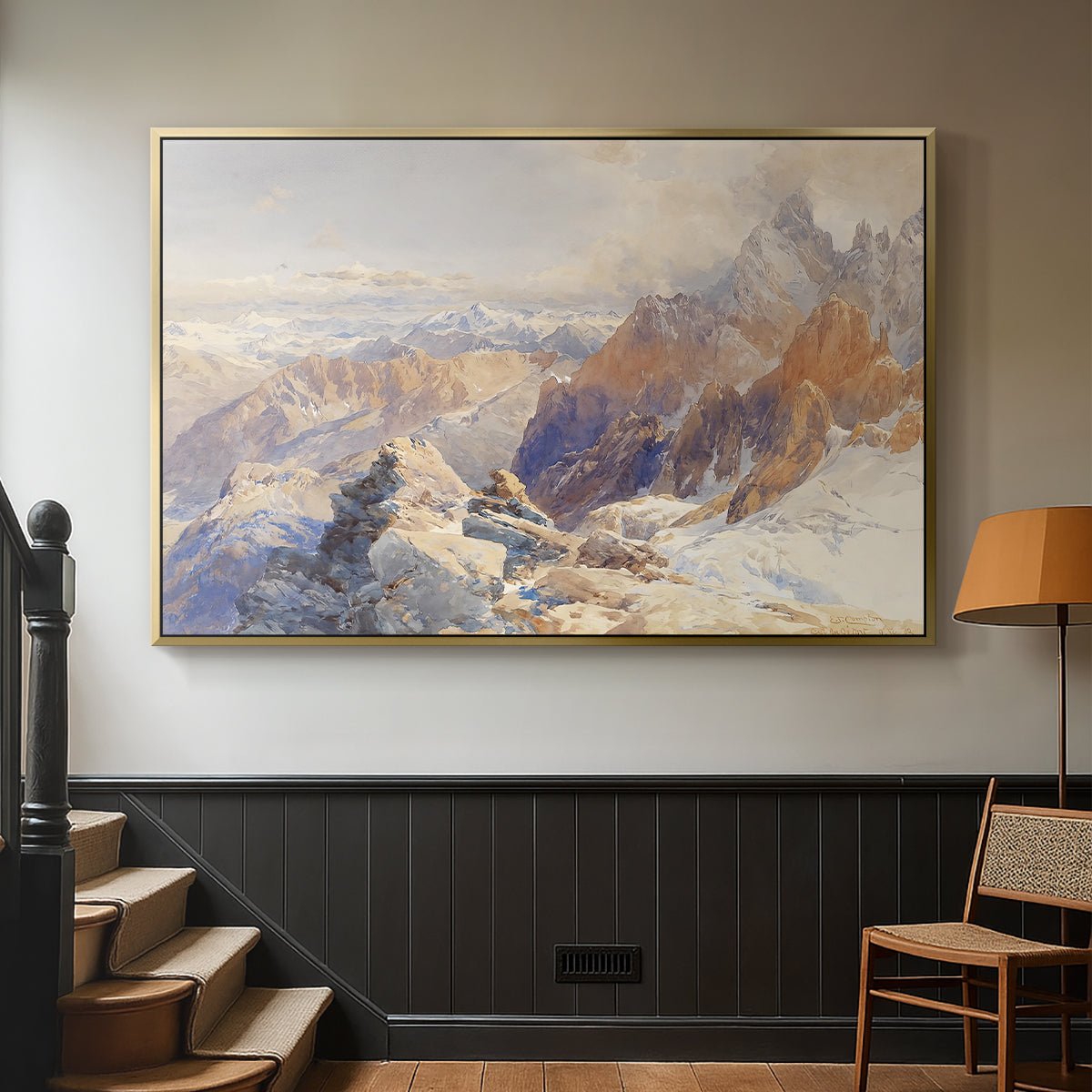 Gold floater framed canvas featuring a rugged mountain pass scene with distant peaks, displayed in a hallway near a staircase.