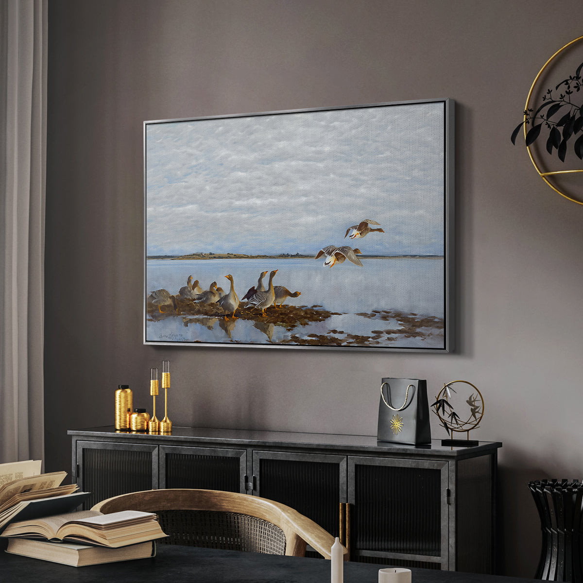 Greylag Geese (Grågäss), 1922 by Bruno Liljefors in a silver floater framed canvas featuring a realistic wildlife scene of geese in calm outdoor environment, displayed above a desk in a dark home office interior.