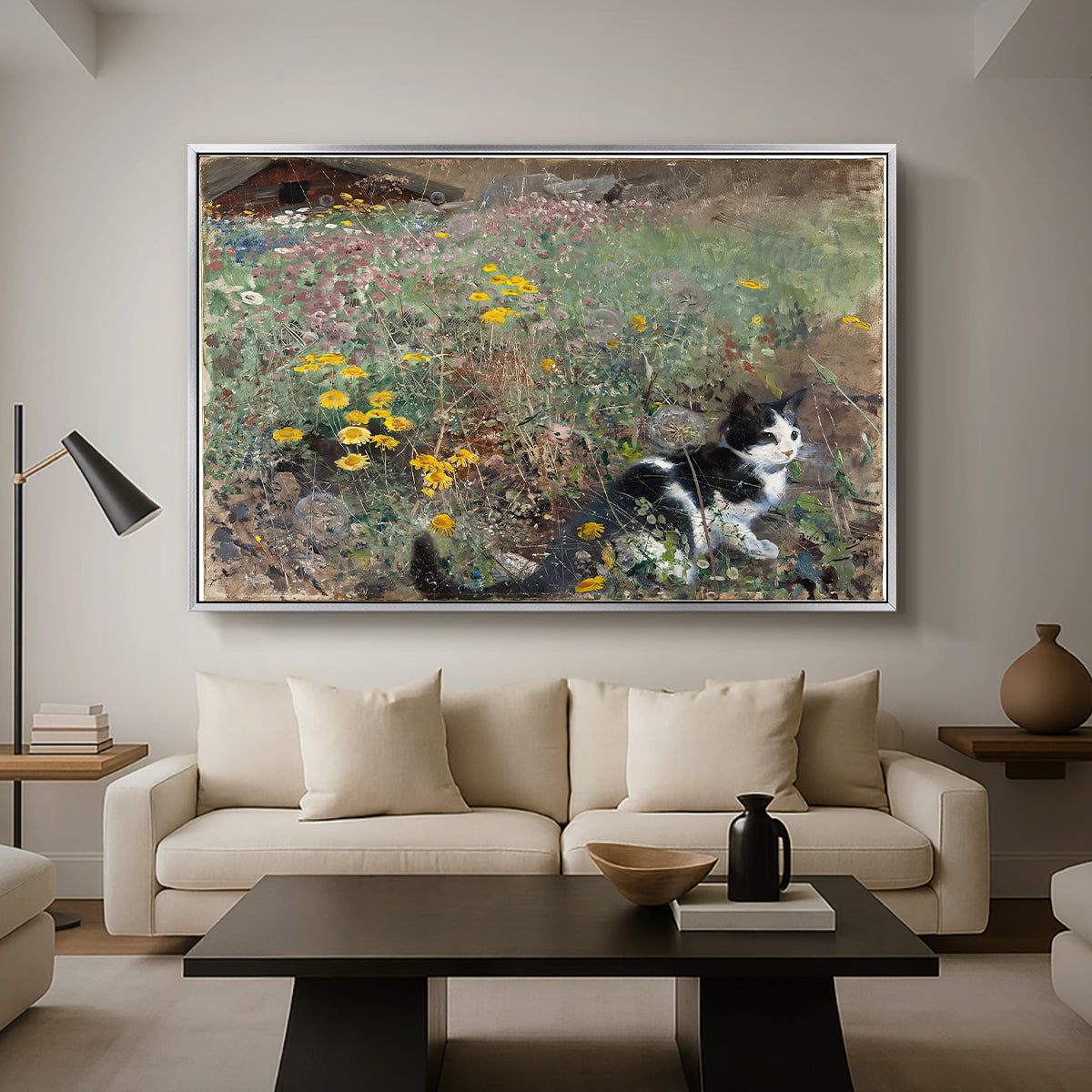 Cat on a Flowery Meadow, 1887 by Bruno Liljefors as a silver floater framed canvas featuring a cat crouching in a meadow filled with wildflowers and greenery, displayed above a sofa in a modern living room.