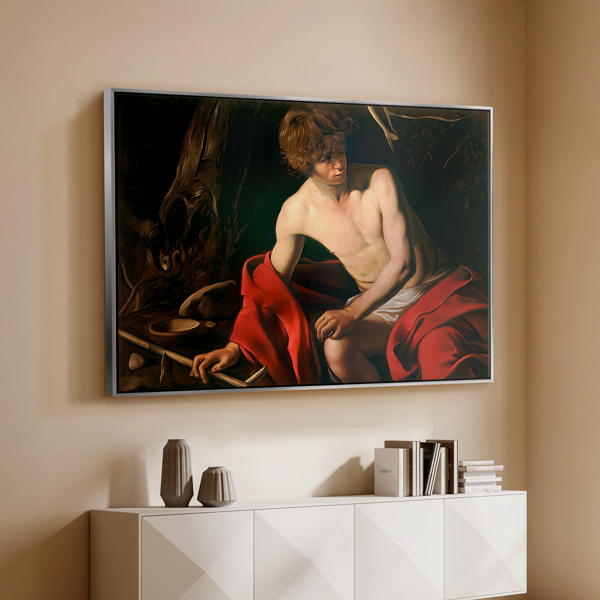 Silver floater framed canvas of Saint John the Baptist in the Wilderness, c. 1603-1604 by Caravaggio, featuring a solitary figure of Saint John resting in natural setting with soft light above a console cabinet in a minimalist entryway.