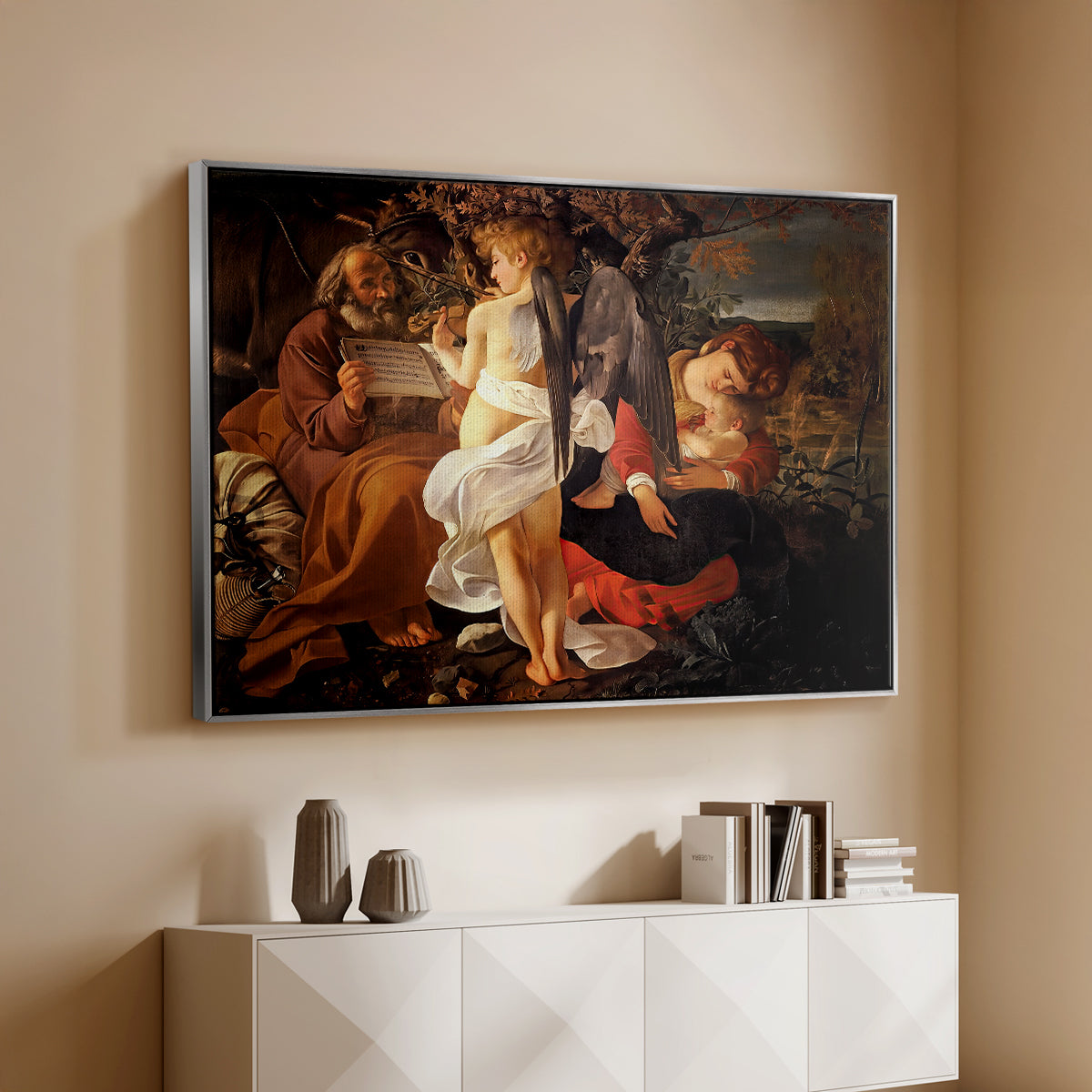 Silver floater framed canvas of Rest on the Flight into Egypt, c. 1597 by Caravaggio, featuring a biblical scene of Mary, Joseph, and infant resting with angel musician above a console cabinet in a minimalist entryway.