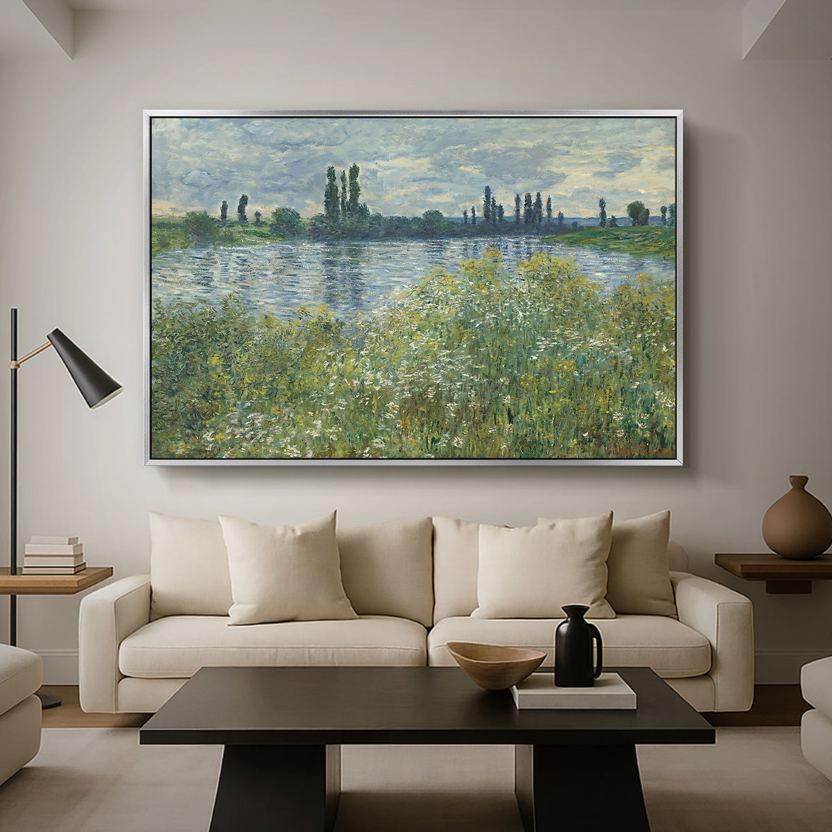 Banks of the Seine, Vétheuil, 1880 by Claude Monet as a silver floater framed canvas featuring a riverbank landscape with water, trees, and distant village buildings, displayed above a sofa in a modern living room.