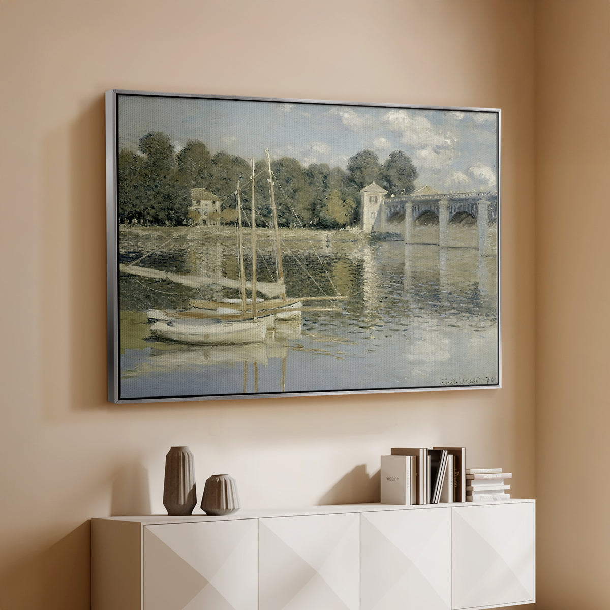 Silver floater framed canvas of The Bridge at Argenteuil, 1874 by Claude Monet, featuring an impressionist river scene with boats passing beneath bridge above a console cabinet in a minimalist entryway.