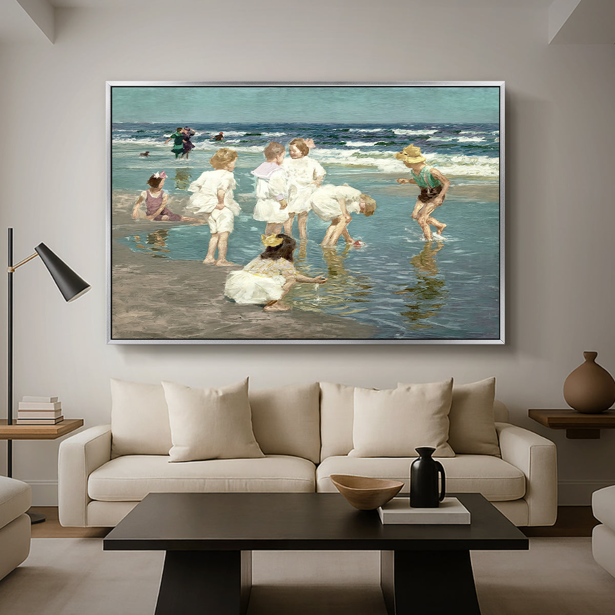 A Holiday, c. 1915 by Edward Henry Potthast as a silver floater framed canvas featuring people relaxing and wading in shallow ocean water along a sunny beach, displayed above a sofa in a modern living room.