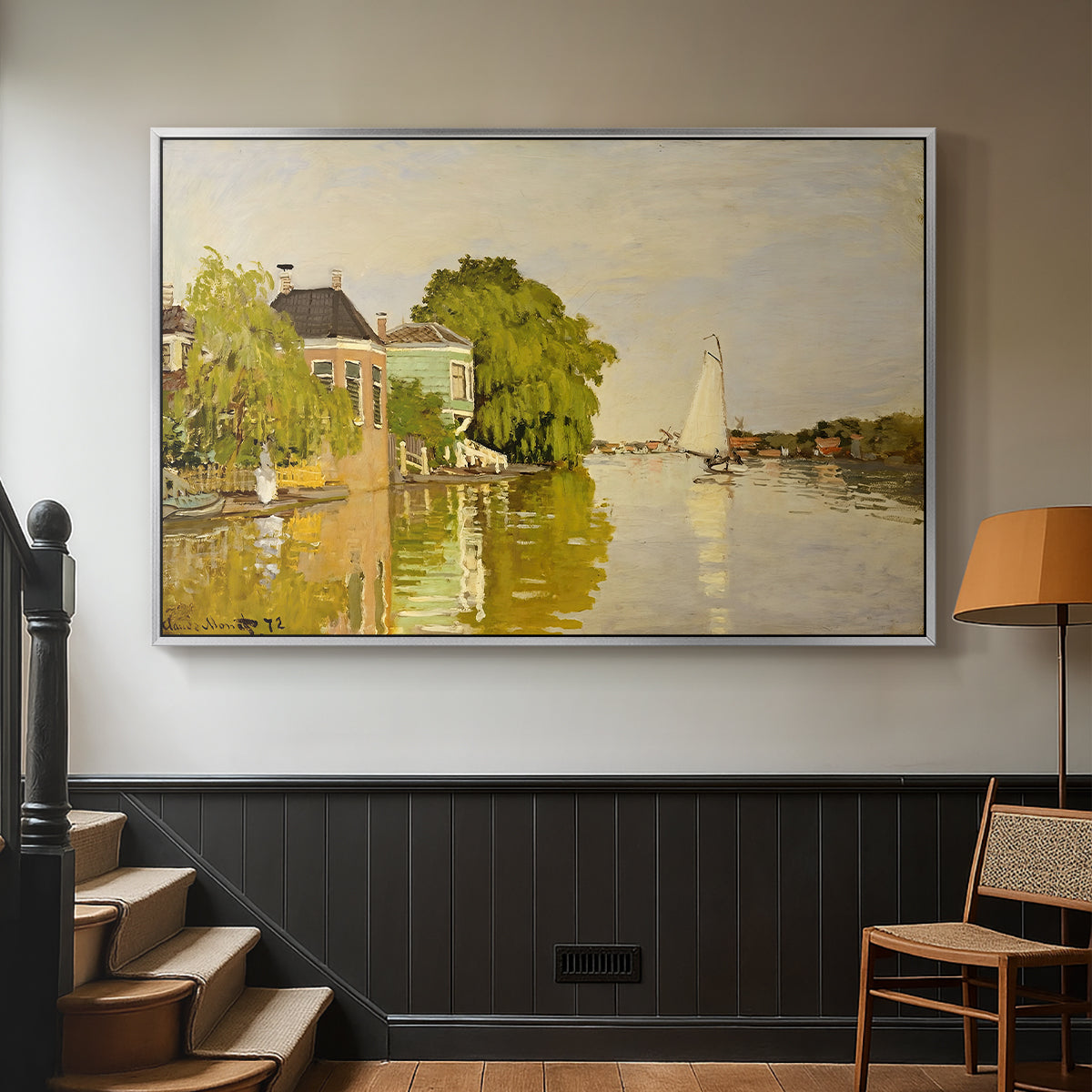 Silver floater framed canvas featuring a peaceful village scene with houses bordering water, displayed in a hallway near a staircase.